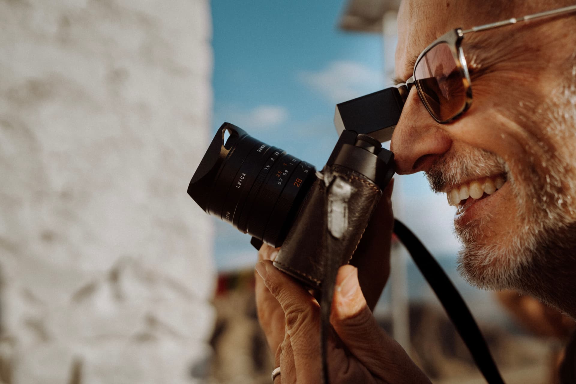 A photographer framing a shot through a rangefinder camera in bright daylight