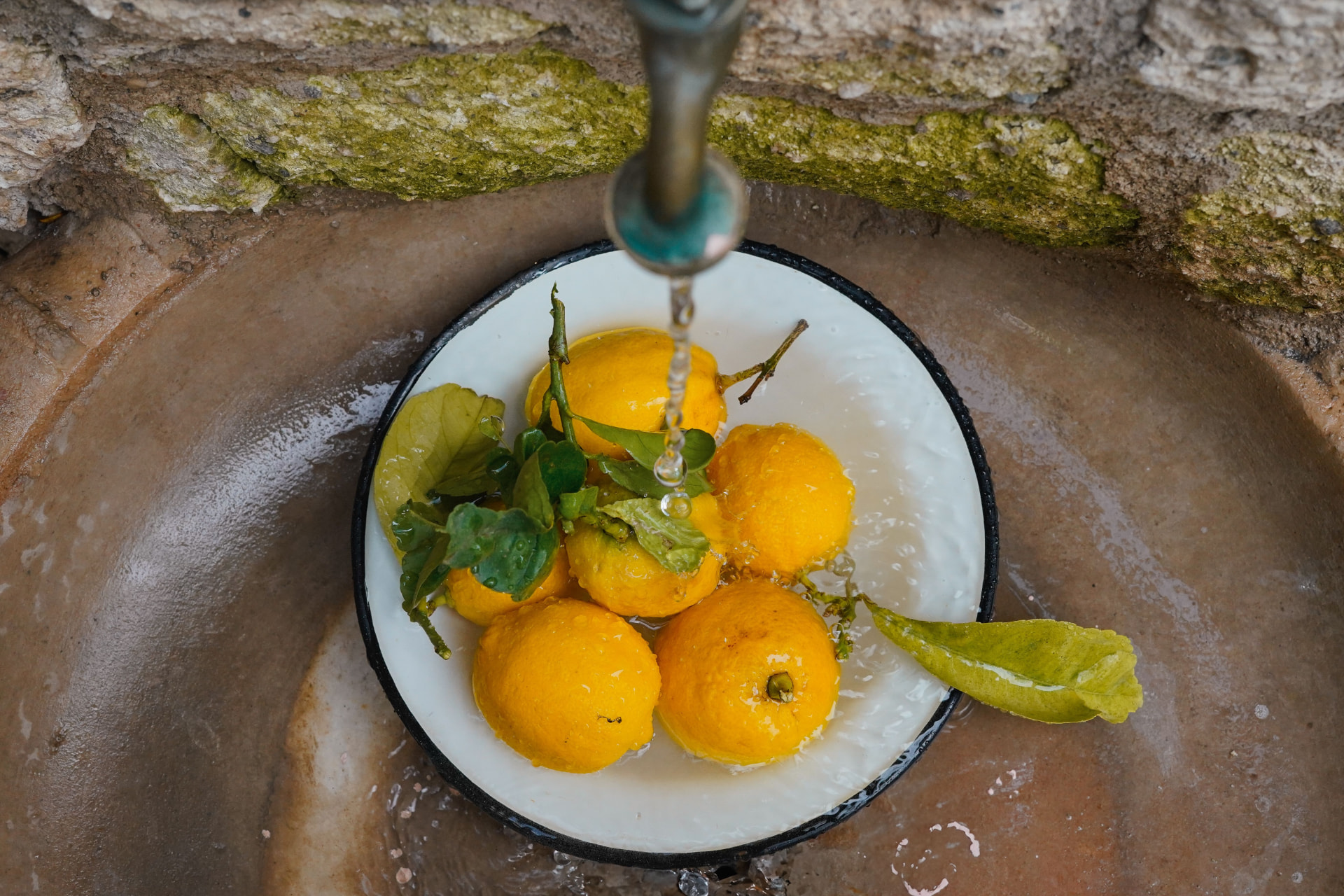 Fresh citrus fruit being rinsed under running water in a stone basin