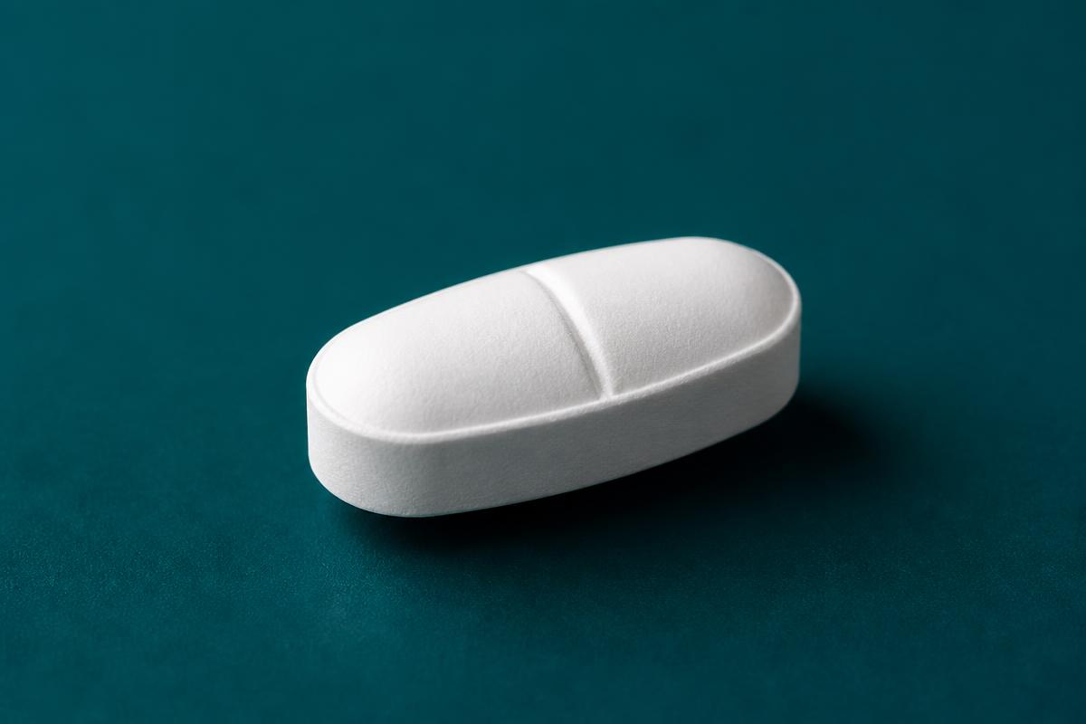 A single white modafinil tablet on a deep teal surface